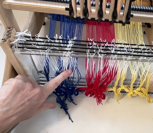 een hand wijst aan hoe de schering door de hevels is geregen