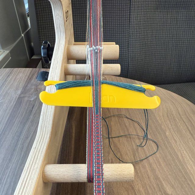 inkle loom in de trein met erop een band in rood en groen