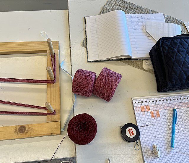 scheerraam, bolletjes garen, meetlint en aantekenschriftje op een werktafel